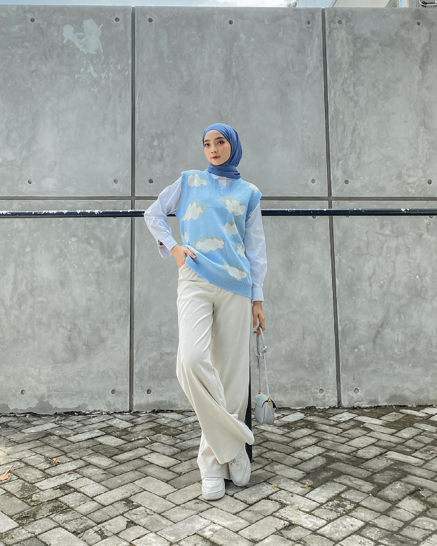 Wanita Indonesia mengenakan hijab warna biru dan padanan rompi rajut motif awan warna biru muda.