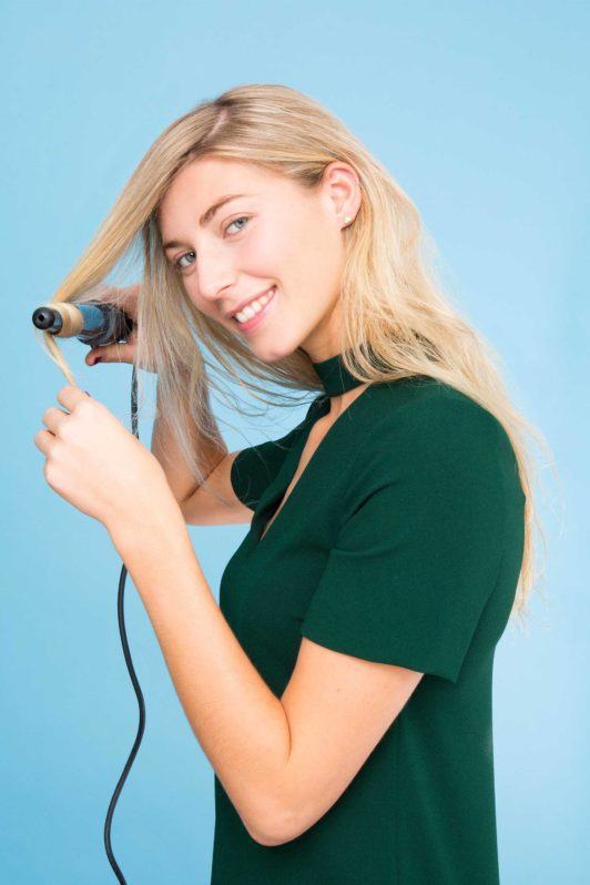 a woman iron curling her blonde hair
