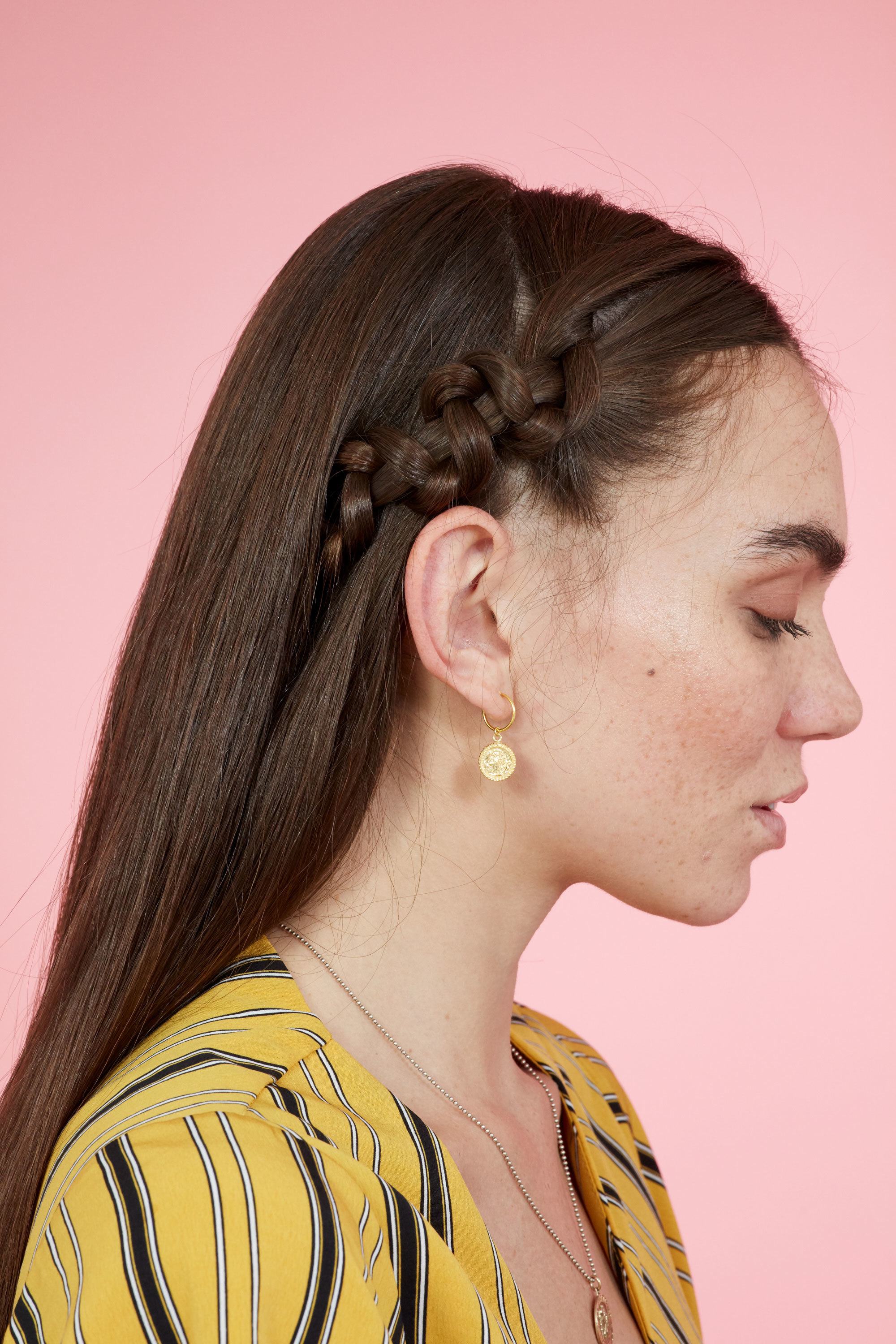 Braids for long hair: Woman with straight dark brown hair with accent snake braid on one side wearing a yellow top against a pink backdrop.