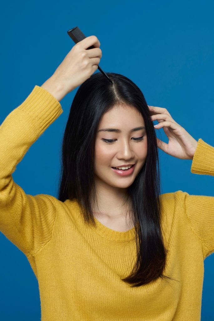 Asian woman parting hair at the center with a comb
