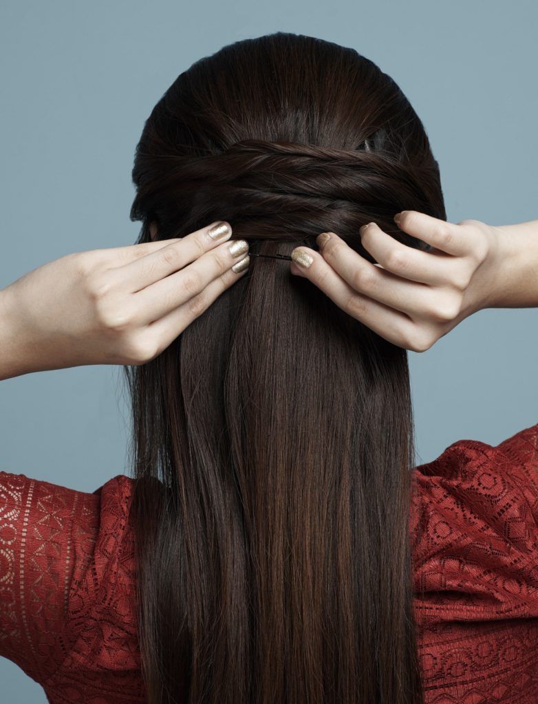 Half up criss cross: Closeup shot of the back of a woman's head with hair being styled into half up criss cross against a blue background