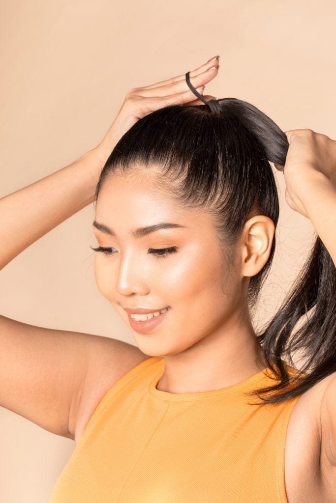Sleek and fierce ponytail: Closeup shot of an Asian woman tying her long black hair in a ponytail