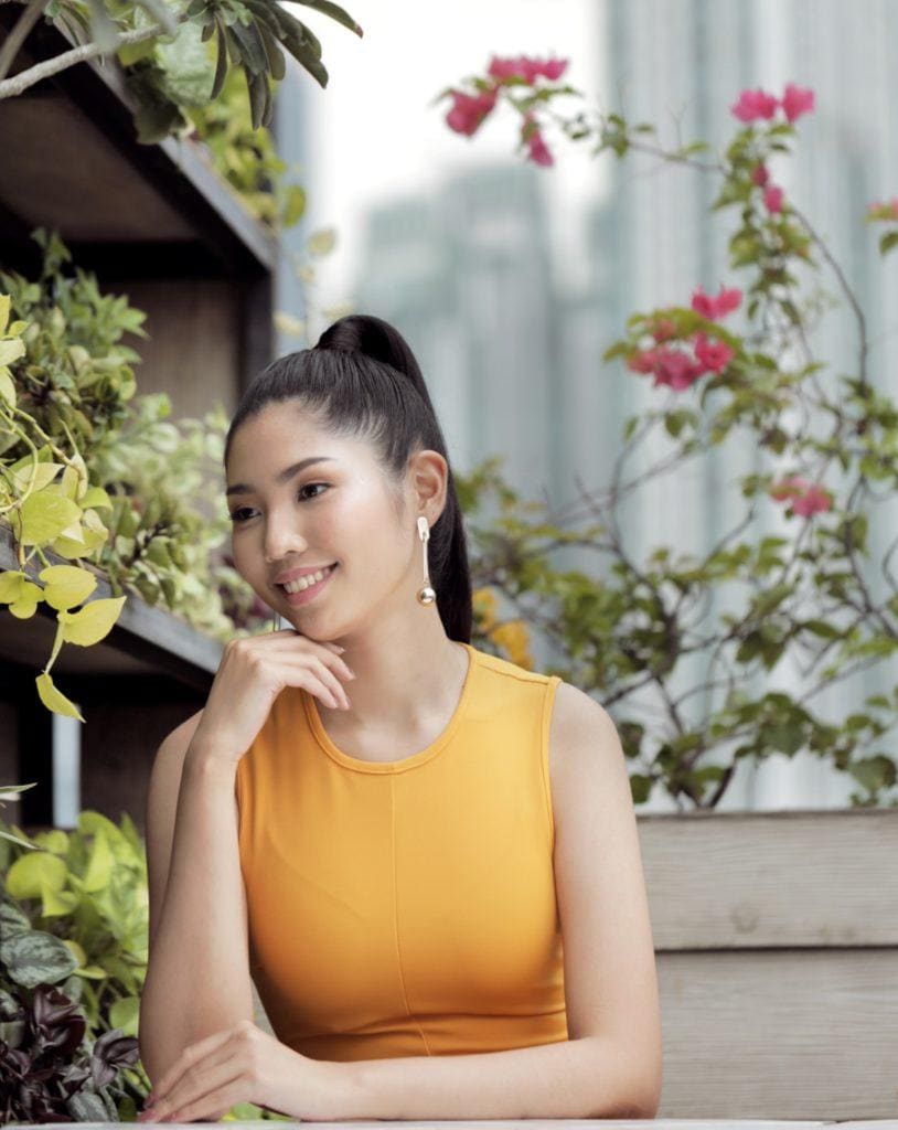Sleek and fierce ponytail: Closeup shot of an Asian woman with long black hair in high ponytail wearing a mustard dress on a rooftop lounge
